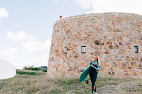 A woman walking with a surf board. Kempt Tower behind her.