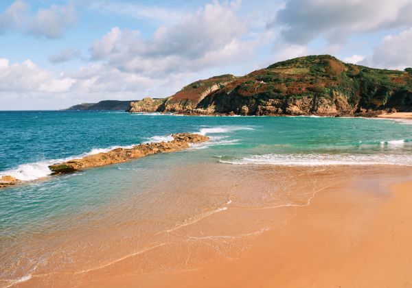 Turquoise sea and golden sandy beach next to cliff tops
