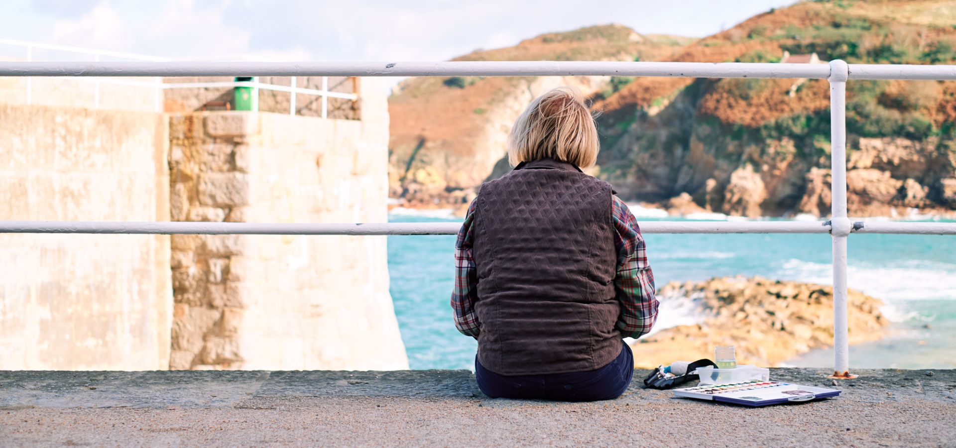 A lady sitting on the pier painting at Greve de Lecq beach