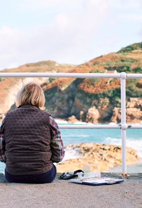 A lady sitting on the pier painting at Greve de Lecq beach