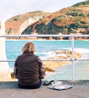 Artist sitting on pier looking out to sea at Greve de Lecq
