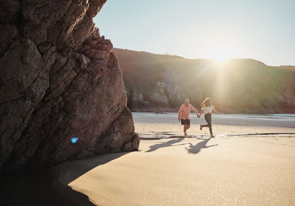A mature couple running leisurely on the beach at Plemont