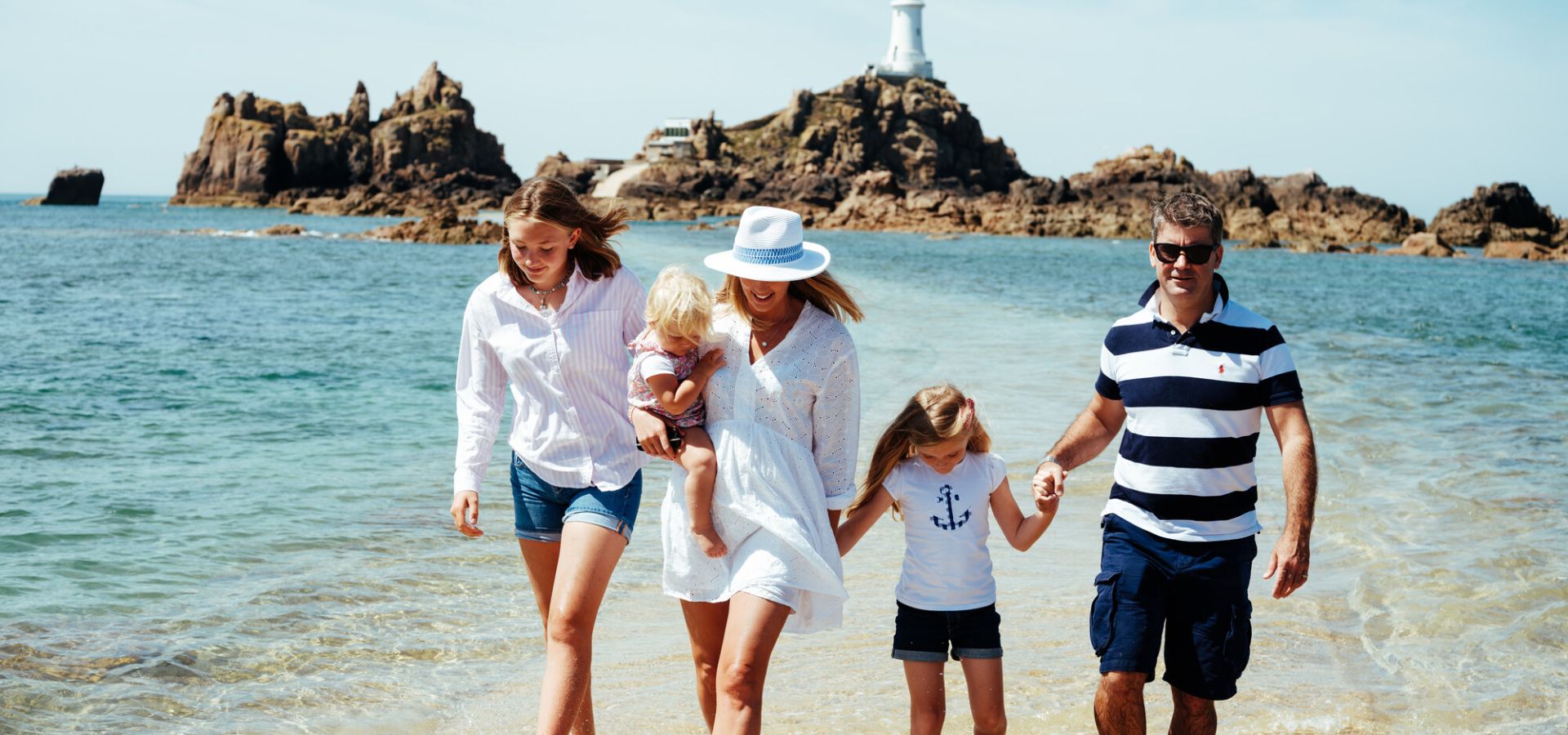 Family walking in shallow water on causeway from Corbiere lighthouse.