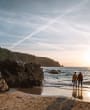 A couple stand at the shoreline as they admire the sunset over Plu00e9mont Bay