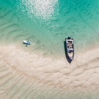 Arial shot of Les Minquiers, Jersey, with turquoise waters, a boat and paddle board