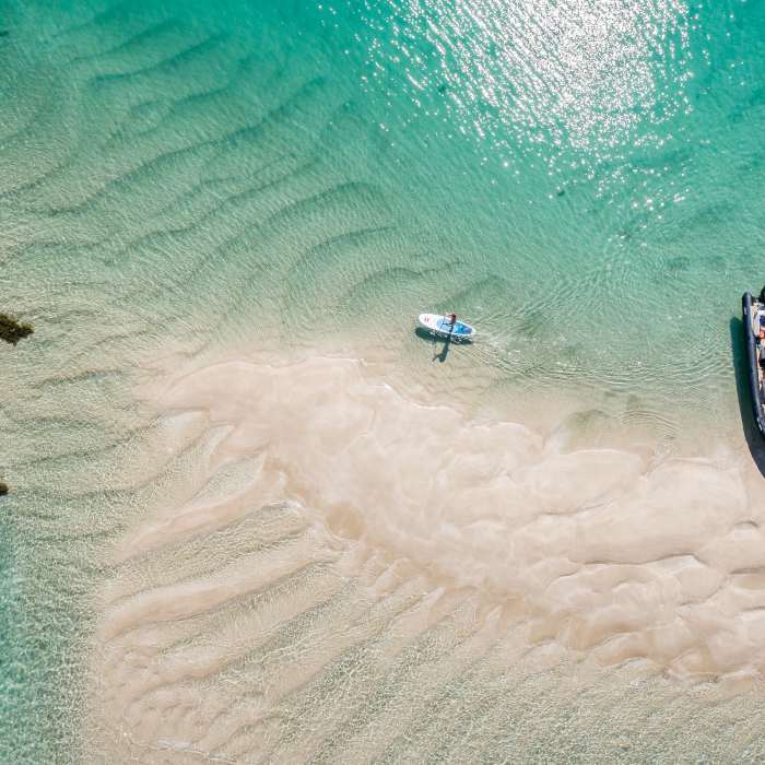 Arial shot of Les Minquiers, Jersey, with turquoise waters, a boat and paddle board