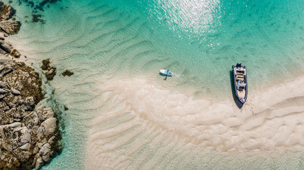 Arial shot of Les Minquiers, Jersey, with turquoise waters, a boat and paddle board