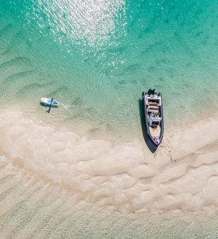 Arial shot of Les Minquiers, Jersey, with turquoise waters, a boat and paddle board