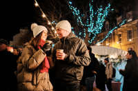 Couple smiling each other. They are wearing warm, wooly, coats are are surrounded by people and bright Christmas lights.