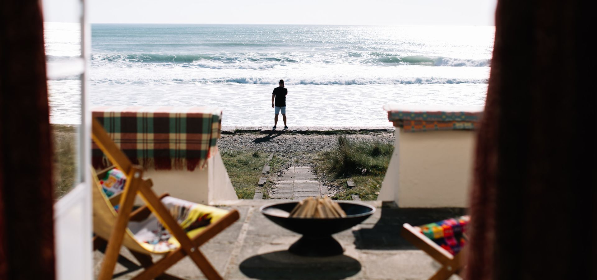 A man stands looking out to sea in the distance.