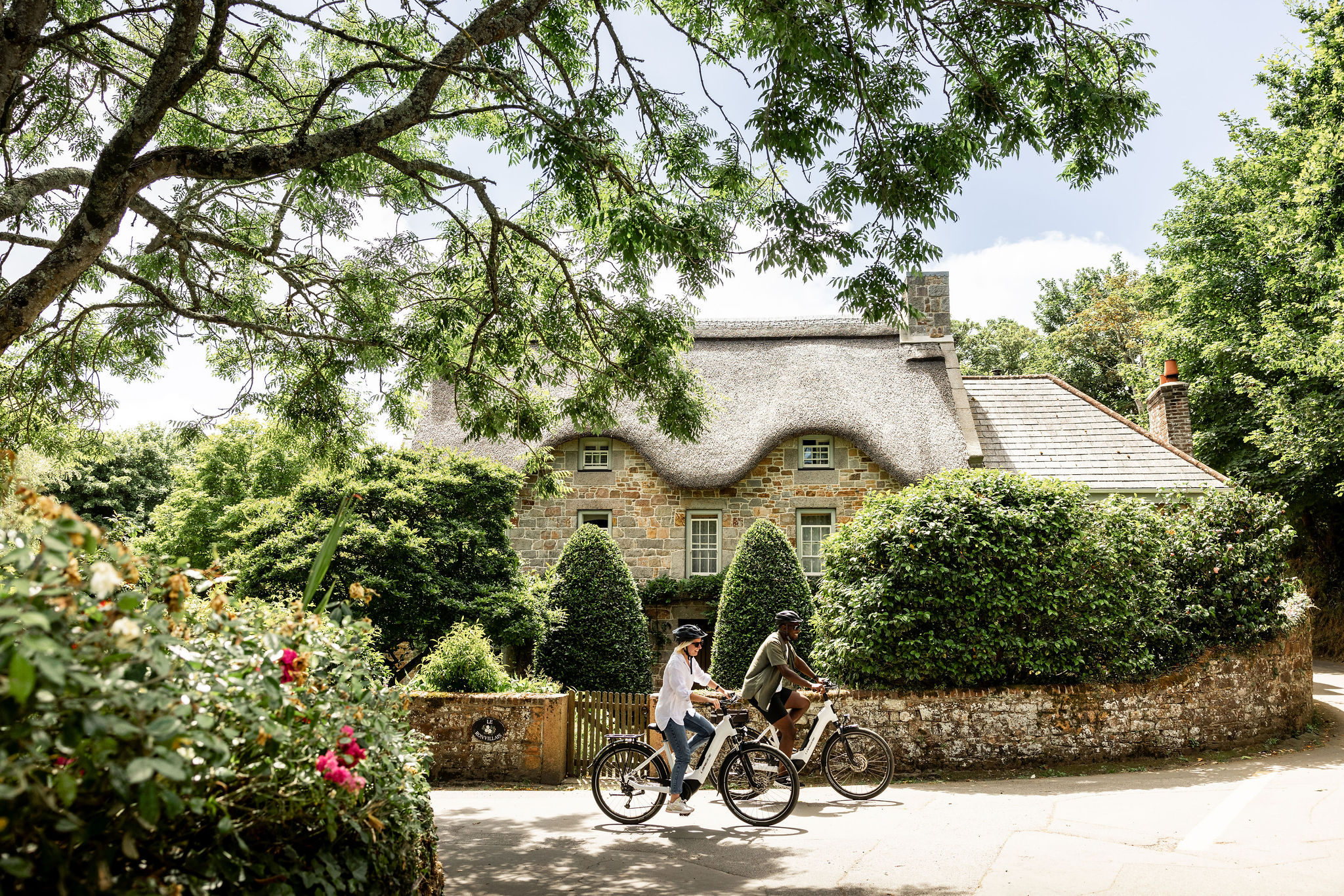 Young couple cycling in the country lanes of Jersey. A pretty thatched cottage cane be seen in the background