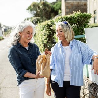Two women picking up Jersey Royal potatoes from a roadside honesty box in Jersey