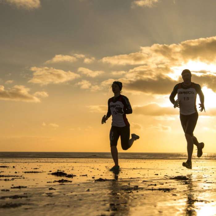 two people running on the beach at sunset